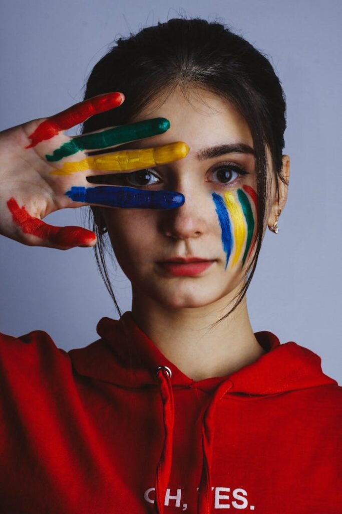 Woman with colorful face paint and hand art poses in studio.